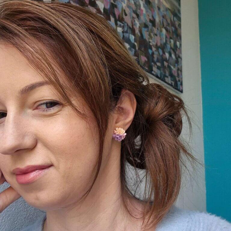 cercei din lut polimeric, buchet cu 3 flori in nuante de violet si crem purtati de o femeie. cerceii sunt pe lobul urechii