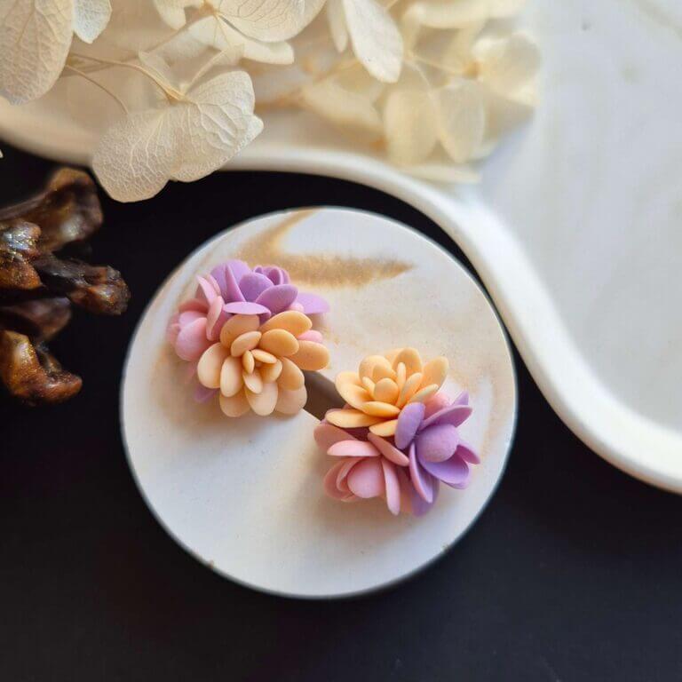 Cercei din lut polimeric, buchet cu 3 flori in nuante de violet, roz si crem asezati pe un suport ceramic. Se pot observa detaliile florilor