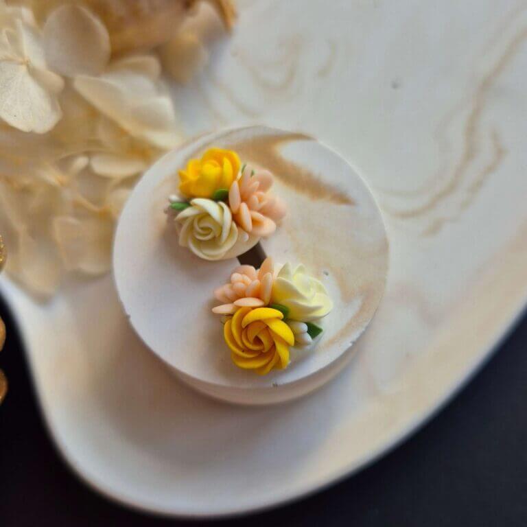 Cercei din lut polimeric, buchet cu 3 flori in nuante de galben si crem asezati pe un suport ceramic. Se pot observa detaliile florilor