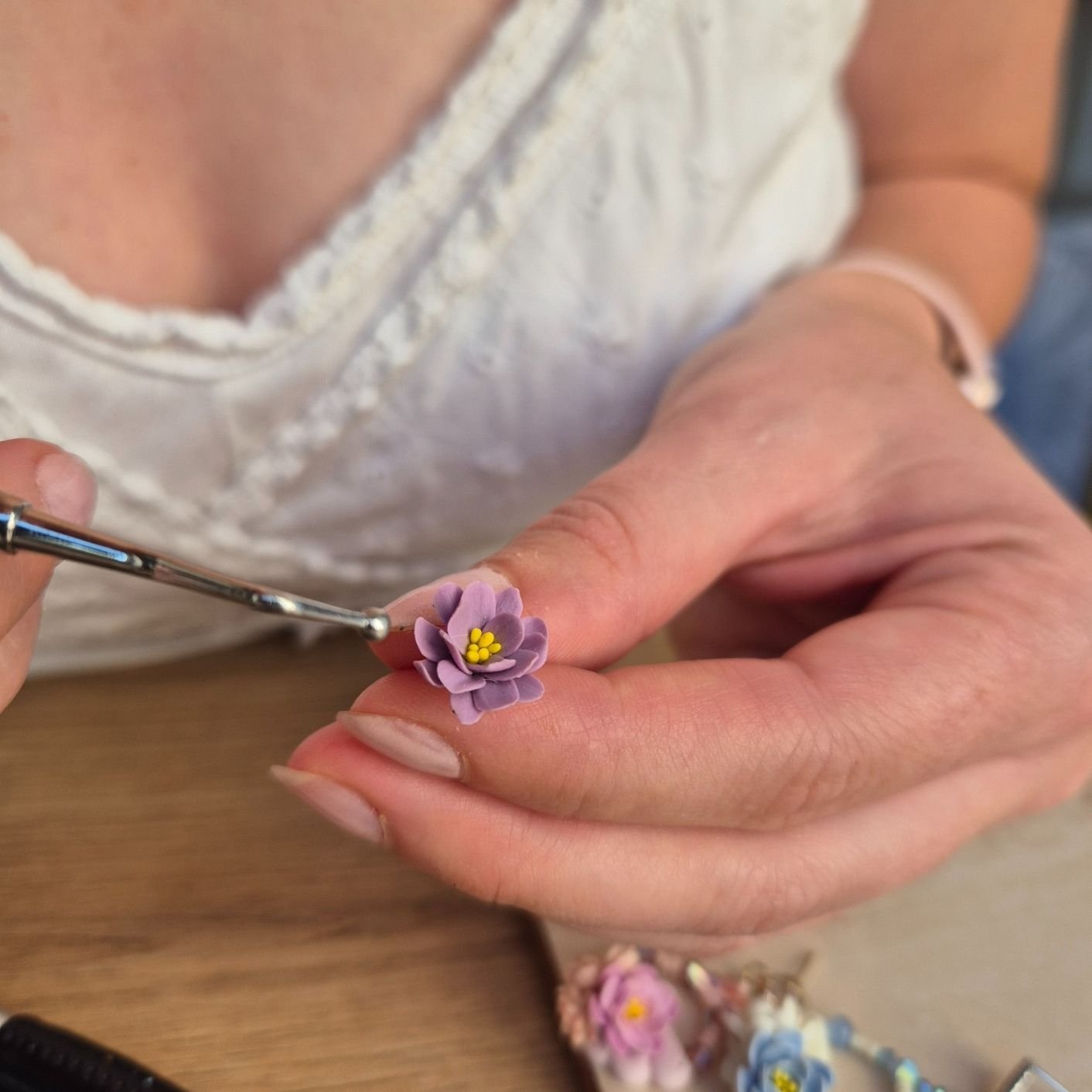 detaliu cu mani lucrand o floare din lut polimeric violet
