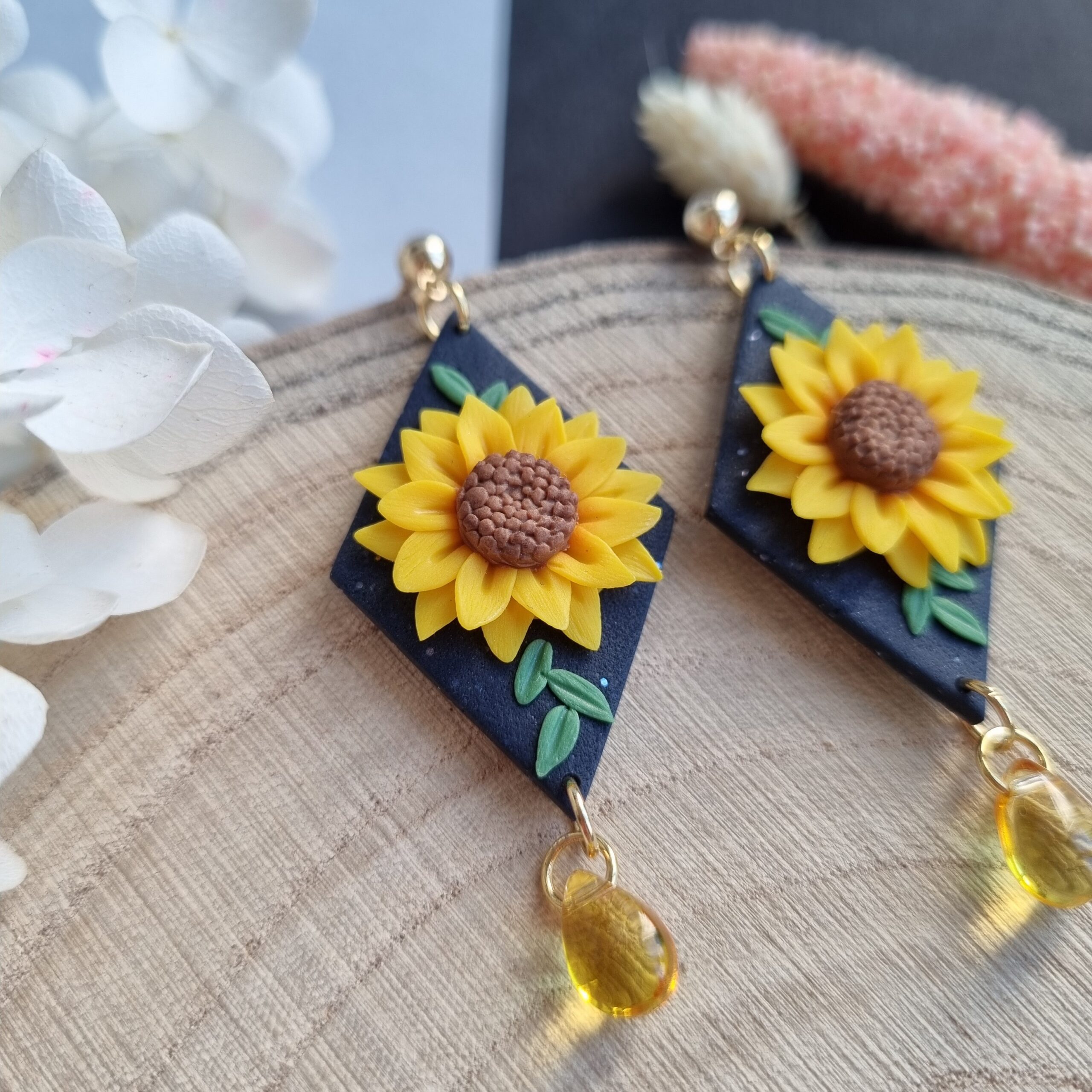 Cercei cu floarea soarelui din lut polimeric si cristale galbene. Se poate observa detaliul din mijlocul florii si cateva frunzulite care sunt asezate in jurul florii, pe baza inchisa la culoare. Bijuteriile sunt asezate pe un platou de lemn