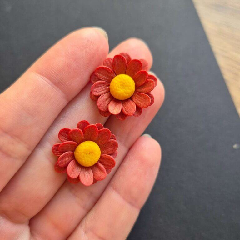 Cercei din lut polimeric reprezentand margarete in culoare rosu-caramiziu. cerceii sunt asezati pe palma pentru a se putea observa dimensiunea