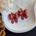 detaliu cercei fundite din lut polimeric, usor sidefat, cu sclipici pe varful panglicilor si cate o margeluta, in aceeasi culoare. cerceii au accesorii metalice aurii si sunt asezati pe un platou ceramic deschis la culoare