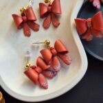 fotografie in care pot fi observati 3 perechi de cercei din lut polimeric, sideafati, rosu caramiziu cu diferite sisteme de prindere pe ureche - platouri si tortite cu bila