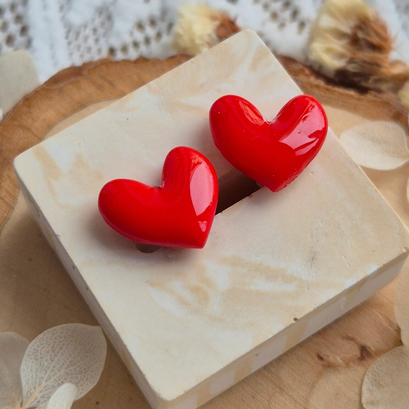 Cercei in forma de inimioara, de purtat pe lobul urechii. Cerceii sunt stralucitori, fiind acoperiti cu un strat de rasina biocompatibila. Asezarea in ureche se face prin intermediul unui platou din otel inoxidabil placat cu aur si fluturas din silicon. Se poate observa cum lumina se reflecta pe suprafata cerceilor. Bijuteria este asezata pe un suport patrat asemanator pietrei.