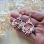 cercei din lut polimeric si cristale, in nuante pale de roz si mov fotografiate pe o palma pentru a se vedea dimensiunea lor