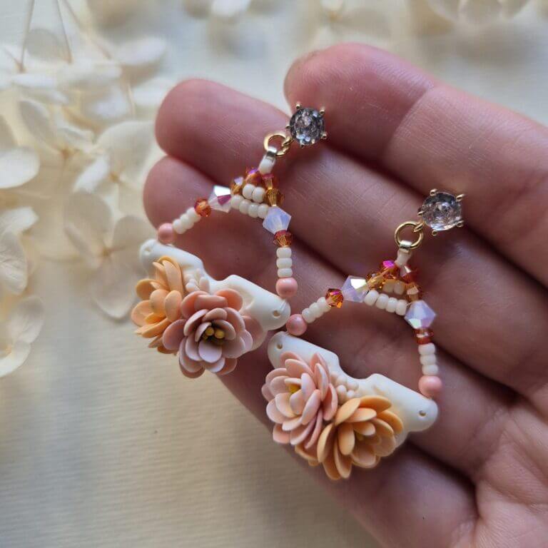 cercei din lut polimeric si cristale, in nuante pale de roz si portocaliu fotografiate pe o mana pentru a se vedea dimensiunea lor