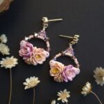 cercei din lut polimeric si cristale, in nuante pale de portocaliu si mov fotografiate pe un fundal negru cu accente de flori uscate