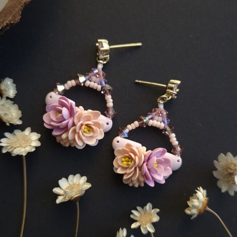 cercei din lut polimeric si cristale, in nuante pale de portocaliu si mov fotografiate pe un fundal negru cu accente de flori uscate