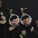cercei din lut polimeric si cristale, in nuante pale de roz si mov fotografiate pe un fundal negru cu accente de flori uscate