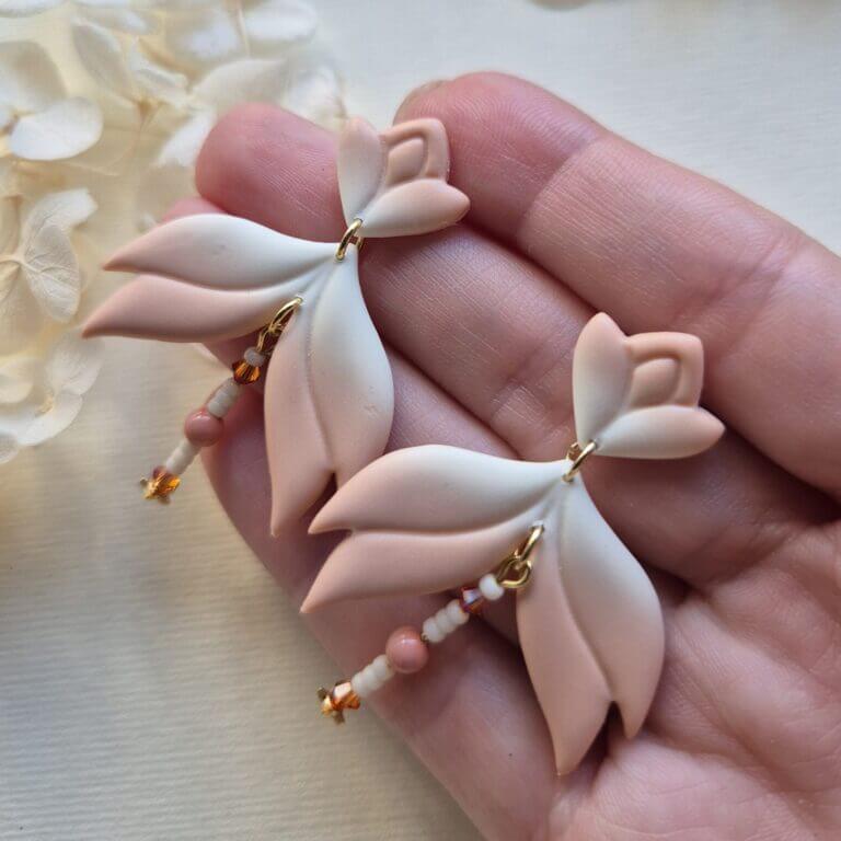 cercei din lut polimeric, catifelati si usori, portocaliu deschis in degrade, avand pe mijloc o piesa mobila cu margele din sticla insirate. cerceii sunt formati din 3 piese legate intre ele cu zale aurii. asezarea in ureche se face cu tortite platou suflate cu aur si sigilate cu un strat de rasina biocompatibila. Partea vizibila a tortitelor are forma de petale. Cerceii sunt tinuti in palma