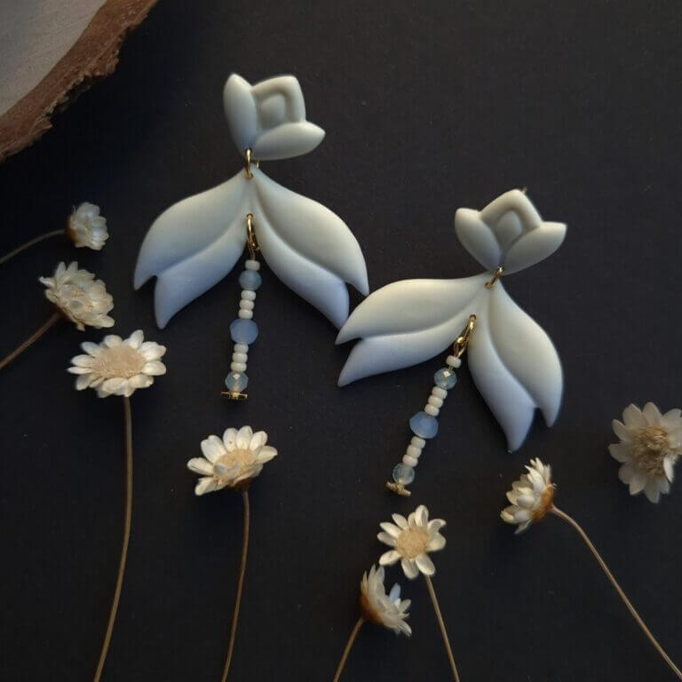 cercei din lut polimeric, catifelati si usori, albastru degrade, avand pe mijloc o piesa mobila cu margele din sticla insirate. cerceii sunt formati din 3 piese legate intre ele cu zale aurii. asezarea in ureche se face cu tortite platou suflate cu aur si sigilate cu un strat de rasina biocompatibila. Partea vizibila a tortitelor are forma de petale. Cerceii sunt fotografiati pe un fundal negru cu decor de flori uscate crem