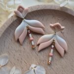 cercei din lut polimeric, catifelati si usori, portocaliu deschis in degrade, avand pe mijloc o piesa mobila cu margele din sticla insirate. cerceii sunt formati din 3 piese legate intre ele cu zale aurii. asezarea in ureche se face cu tortite platou suflate cu aur si sigilate cu un strat de rasina biocompatibila. Partea vizibila a tortitelor are forma de petale. Cerceii sunt asezati pe un platou de lemn