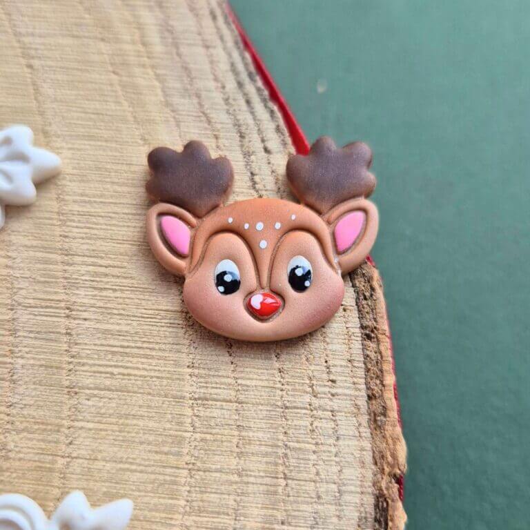 Brosa din lut polimeric reprezentand un ren dragut, cu ochi si nas luciosi, lacuiti cu rasina. detaliile sunt pictate manual. Brosa este asezata pe o felie de lemn