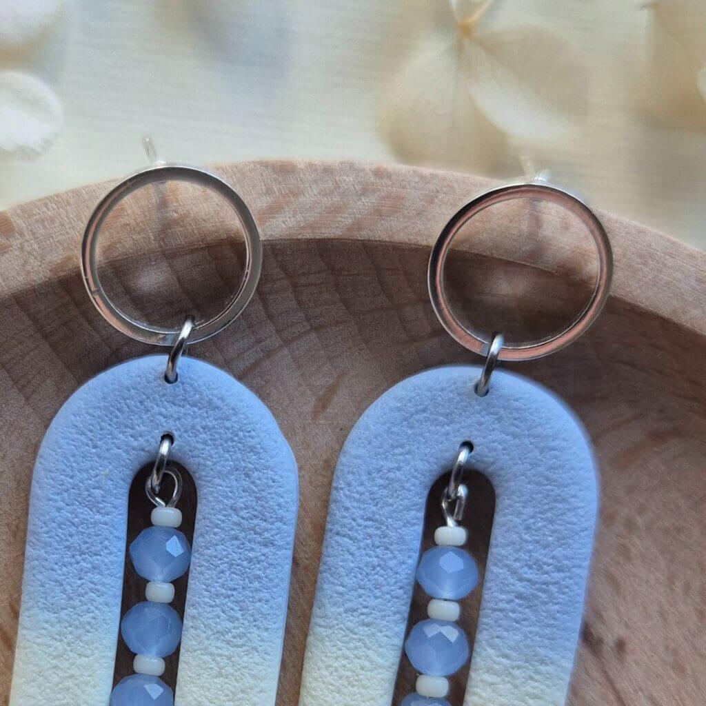 cadru cu un model de cercei din lut polimeric in care se poate observa textura lutului si degradeul albastru crem, cu accent pe tortite din otel inoxidabil