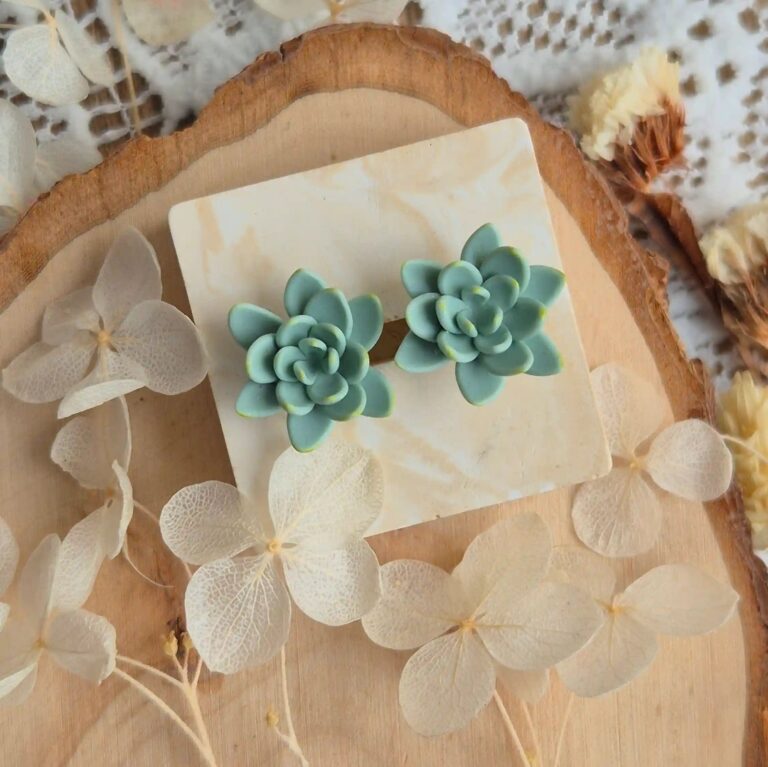 Cercei tip stud cu design de plantă naturală, așezați lângă flori uscate și elemente din lemn, sugerând un stil boho-chic. accesorii sustenabile pentru iubitorii de natură.