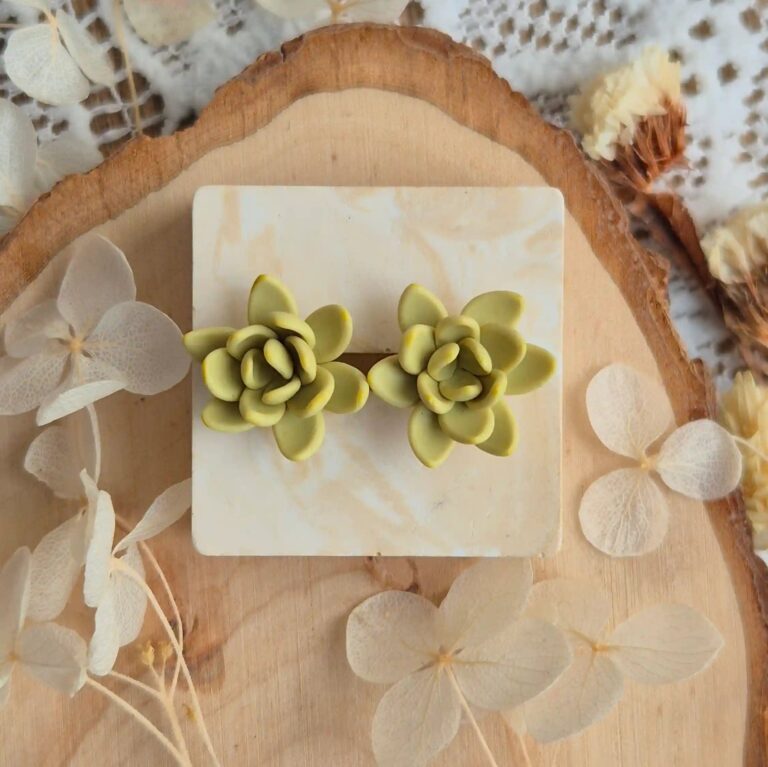 Cercei tip stud cu design de plantă naturală, așezați lângă flori uscate și elemente din lemn, sugerând un stil boho-chic. accesorii sustenabile pentru iubitorii de natură.