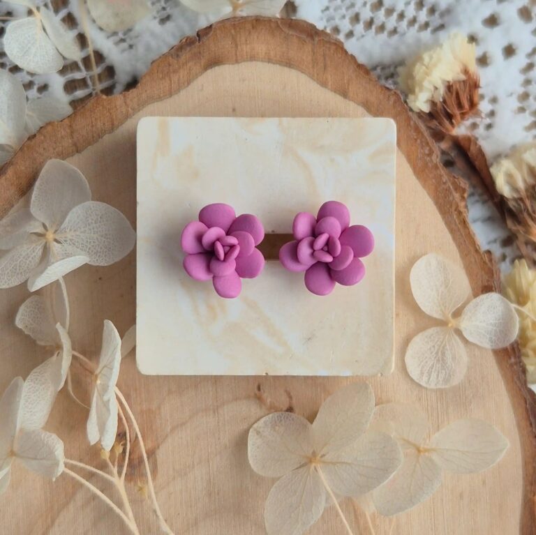 Cercei handmade în formă de floare suculentă mov lavanda, vedere de sus pe un suport de lemn cu flori uscate albe, design botanic elegant.