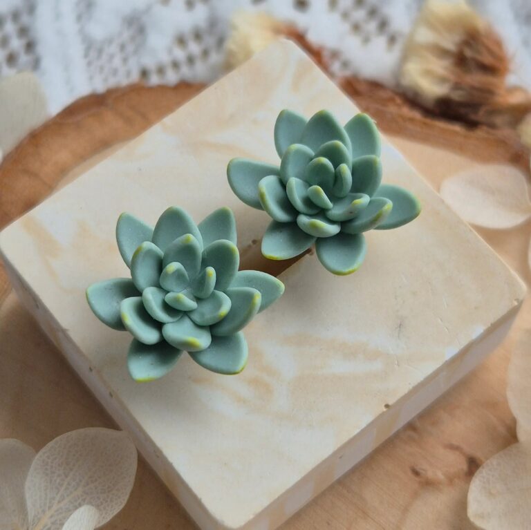 Pereche de cercei lucrați manual în formă de plante suculente Echeveria, de culoare verde mentă cu detalii galbene pe marginea petalelor, prezentați pe un suport decorativ din piatră mată.