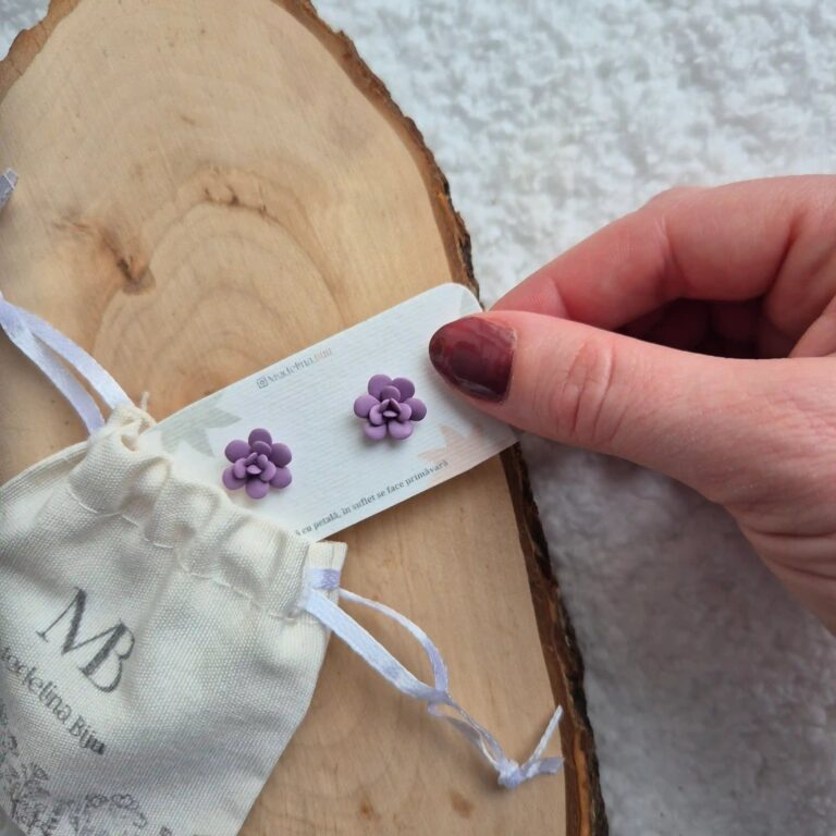 Cercei handmade în formă de floare suculentă mov violet, vedere de sus cu o mana tinand un cartonas personalizat pe care sunt asezati cerceii.