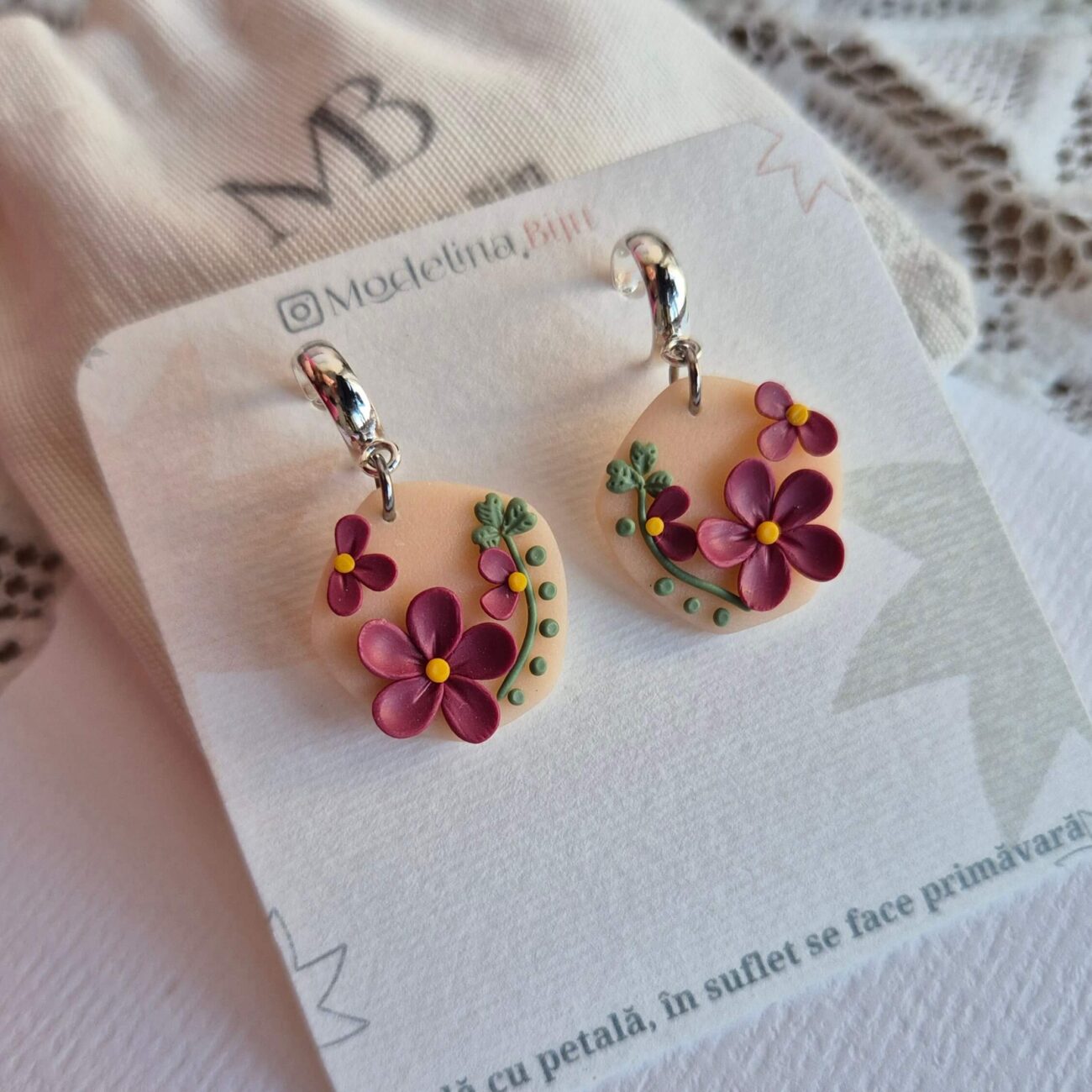 Cercei cu flori magenta,frunze si puncte verzi asezate pe o baza de culoarea piersicii, intr-o forma organica. Cerceii au tortite tip half hoop argintii si sunt asezati pe un cartonas personalizat